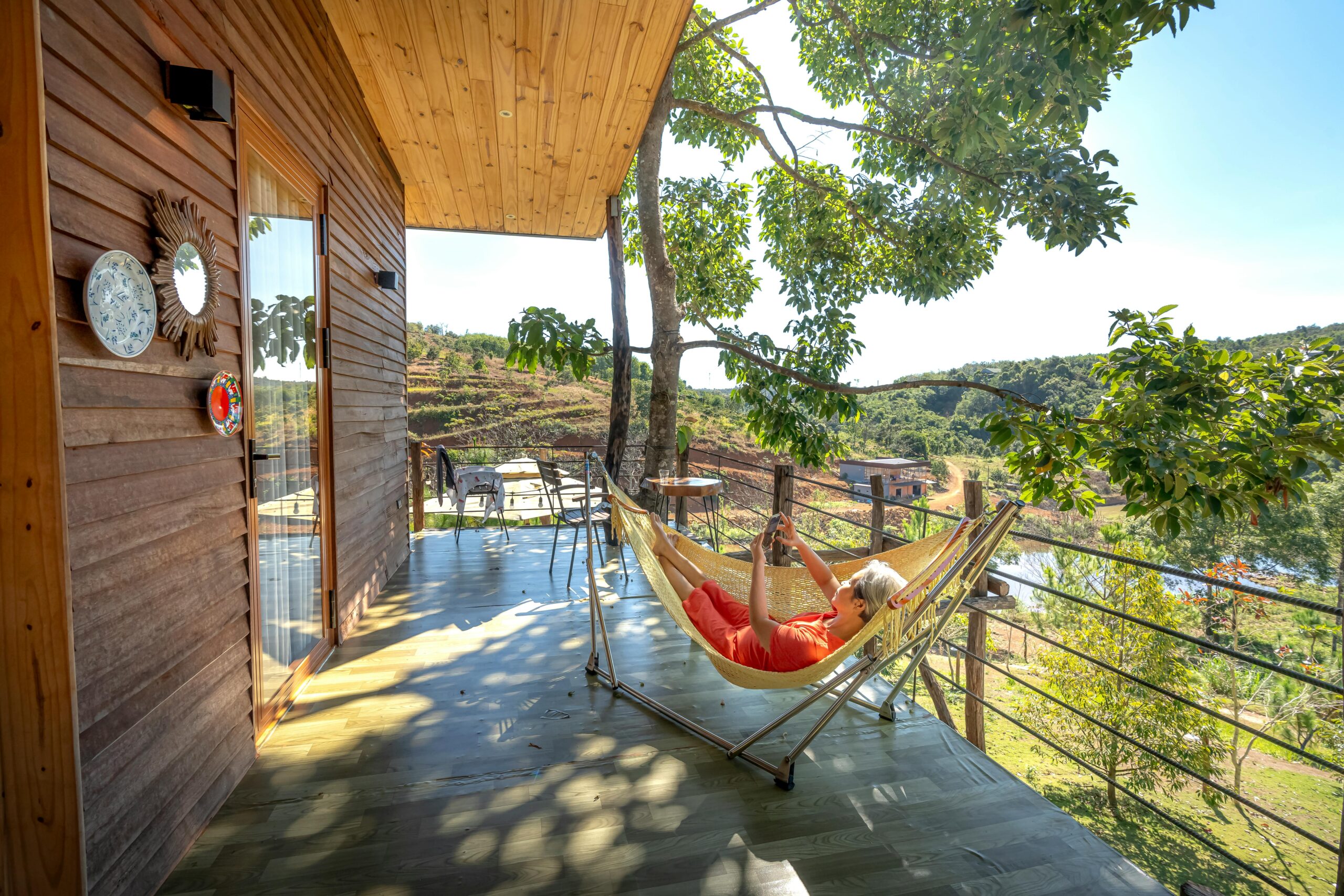 Woman relaxing in a hammock on a wooden terrace overlooking a scenic countryside view.